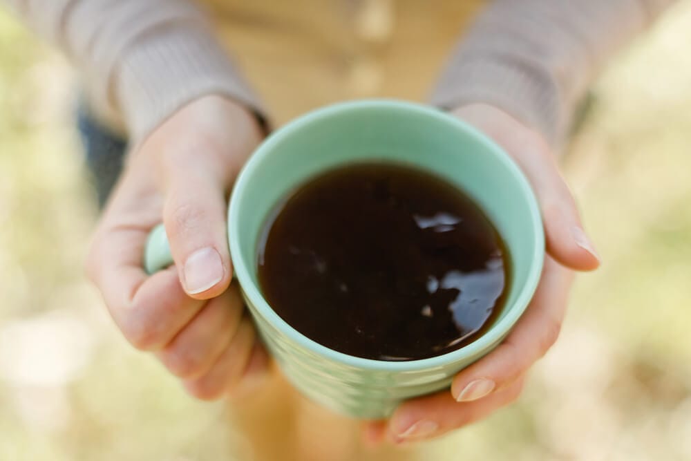 A woman holds a green cup full of tea.