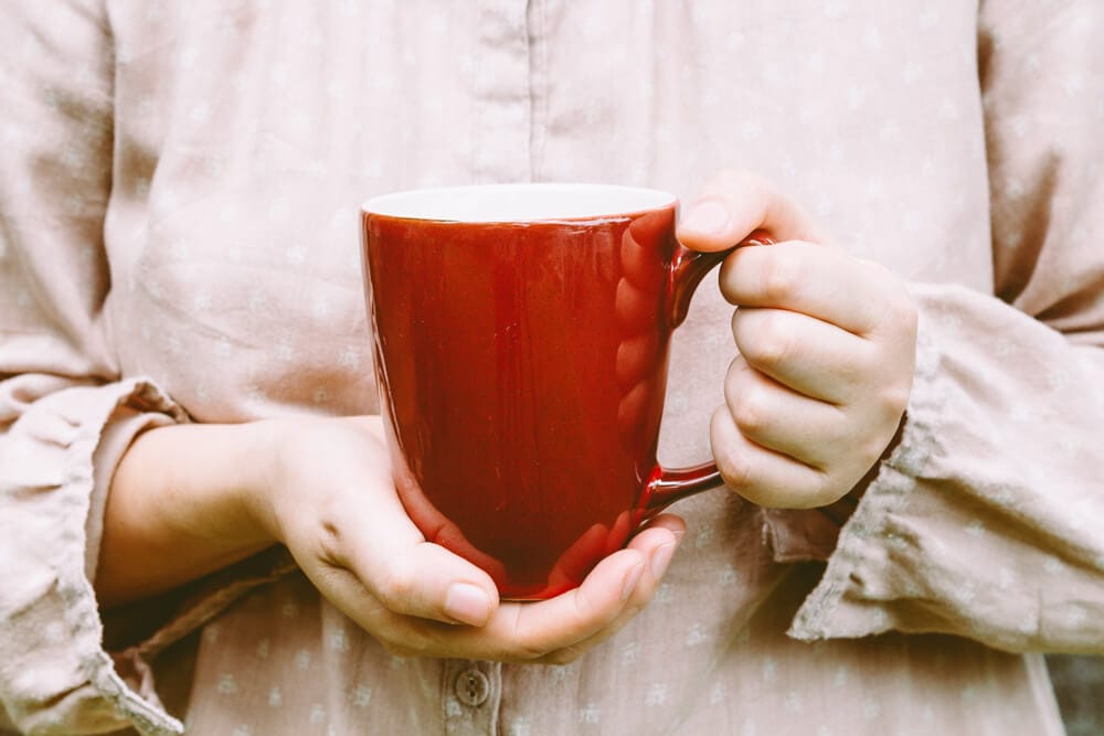 A woman in a pink shirt holding a red mug.