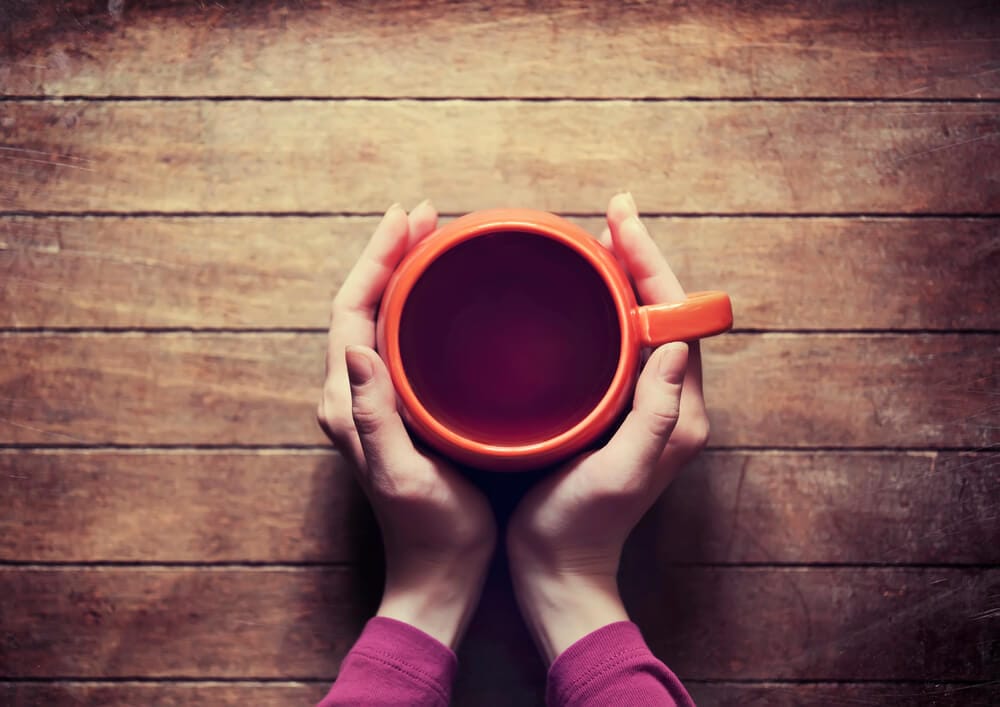 A woman has her hands wrapped around a nice, warm cup of tea.