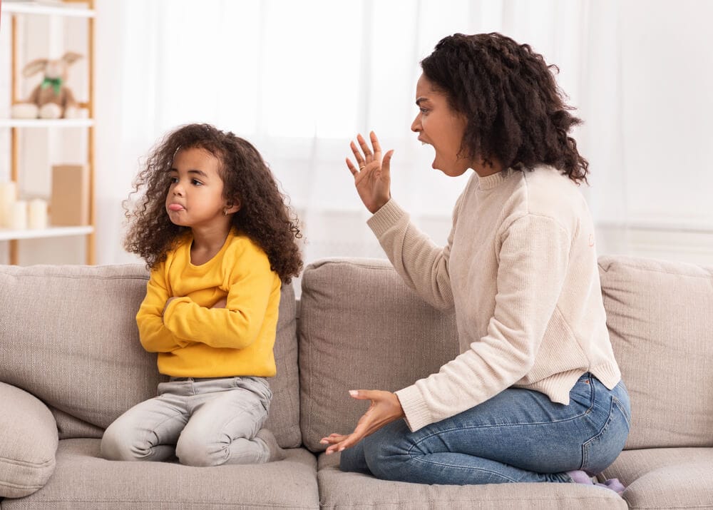 A woman is sitting on the sofa and yelling at her pouting daughter.