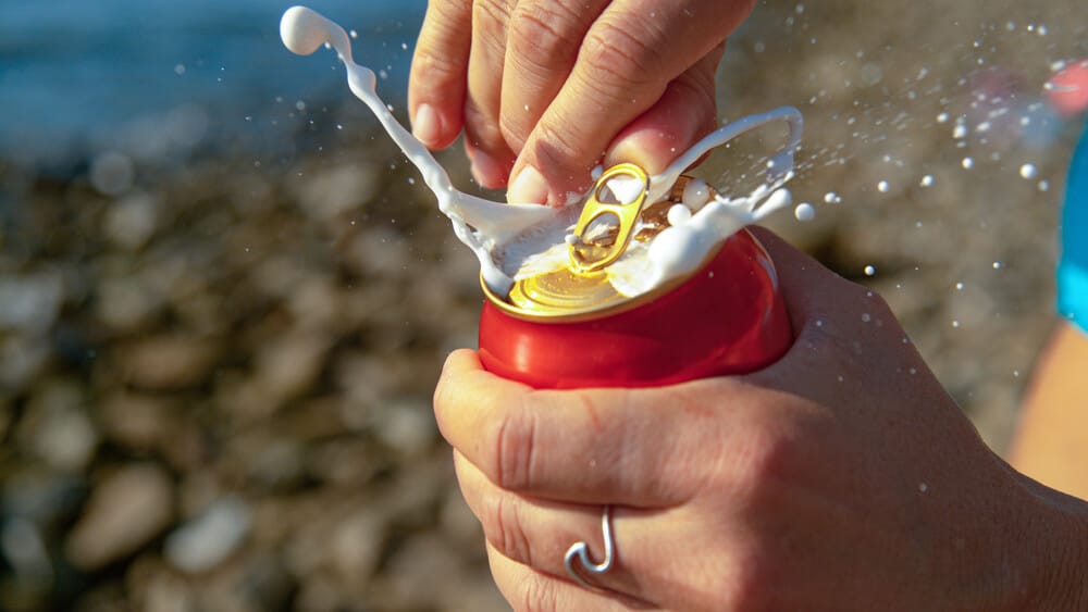 A woman opens a soda can and the drink explodes outwards in a spray.
