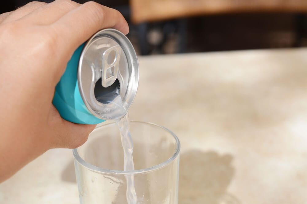 A person pours drink from a soda can into a glass, without an explosion of fizzy liquid.