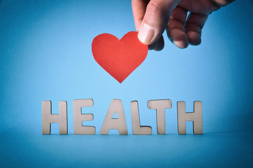 A hand holding a red paper heart above letters spelling out "Health."