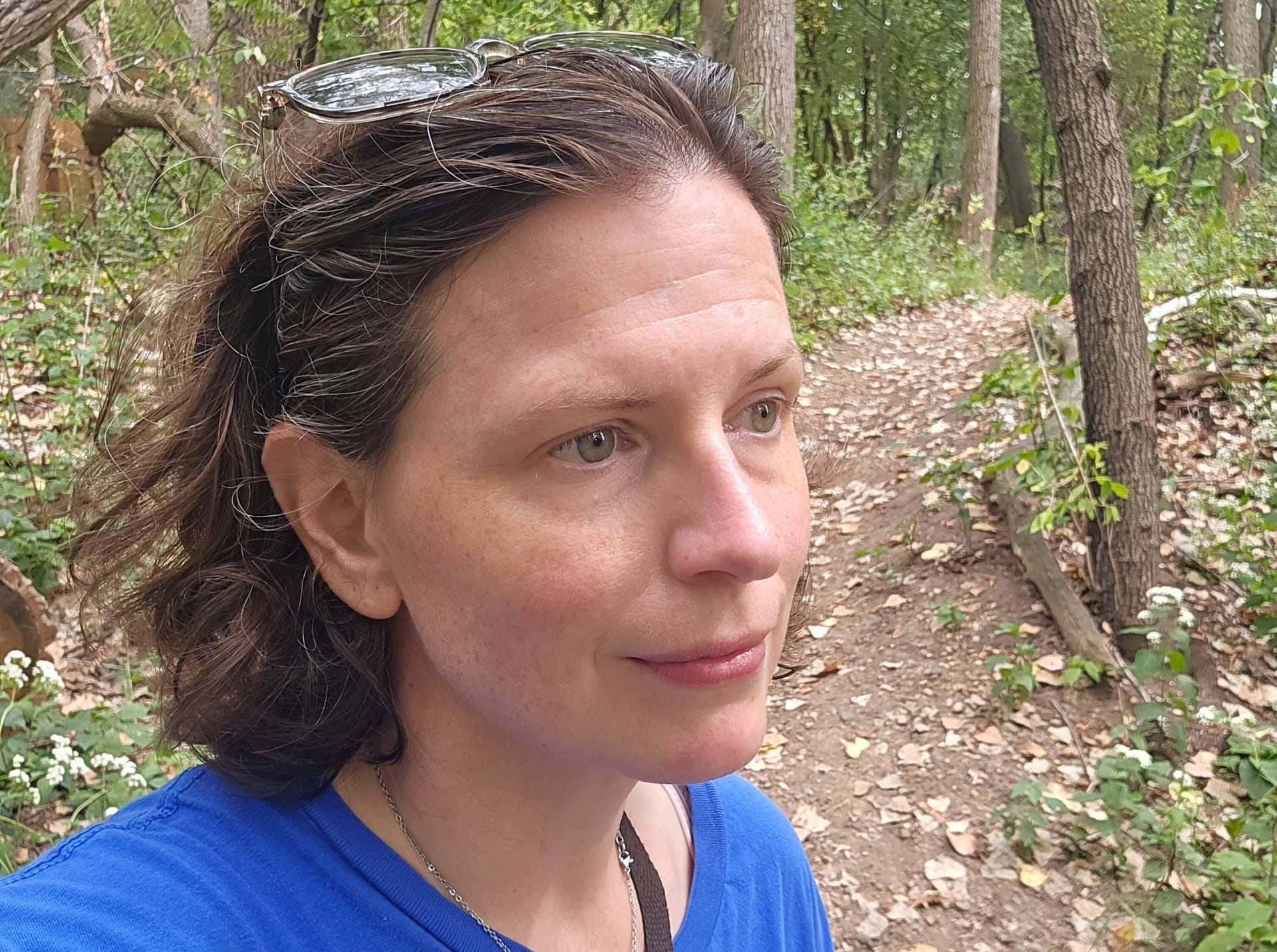 A brown haired woman with hazel eyes looks off camera into the woods.