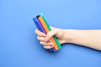 A woman holds six colored markers in her hand.